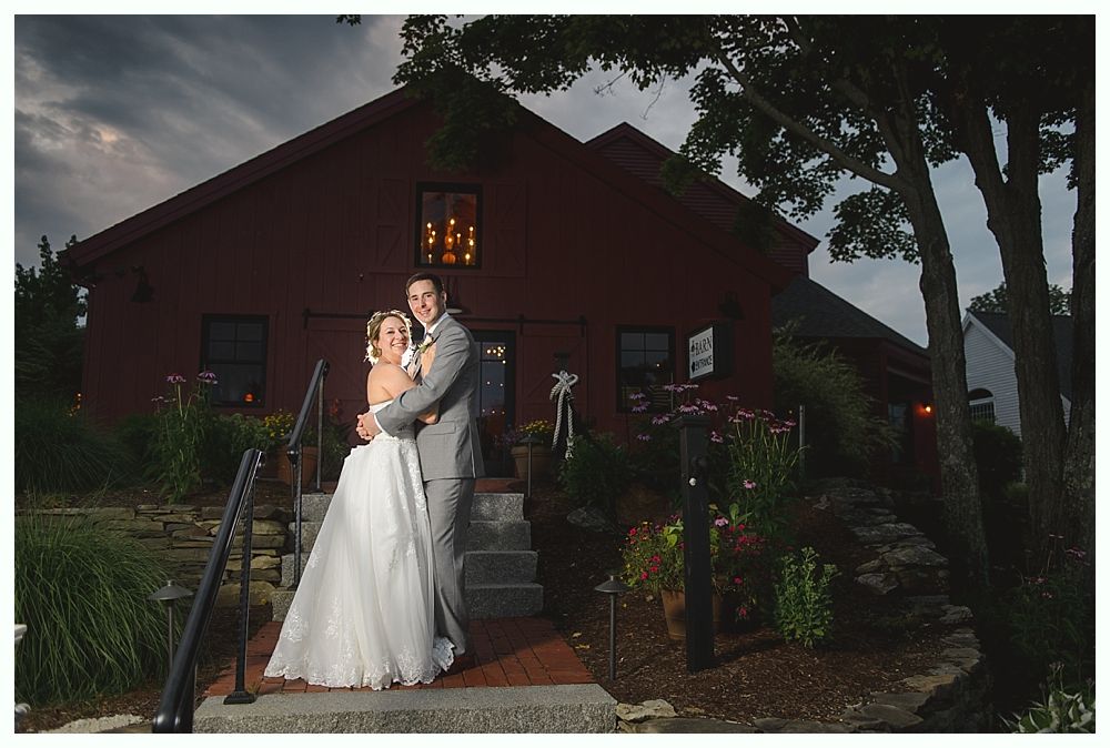 Bride and groom embrace in front of a red building with stairs. Cloudy sky.