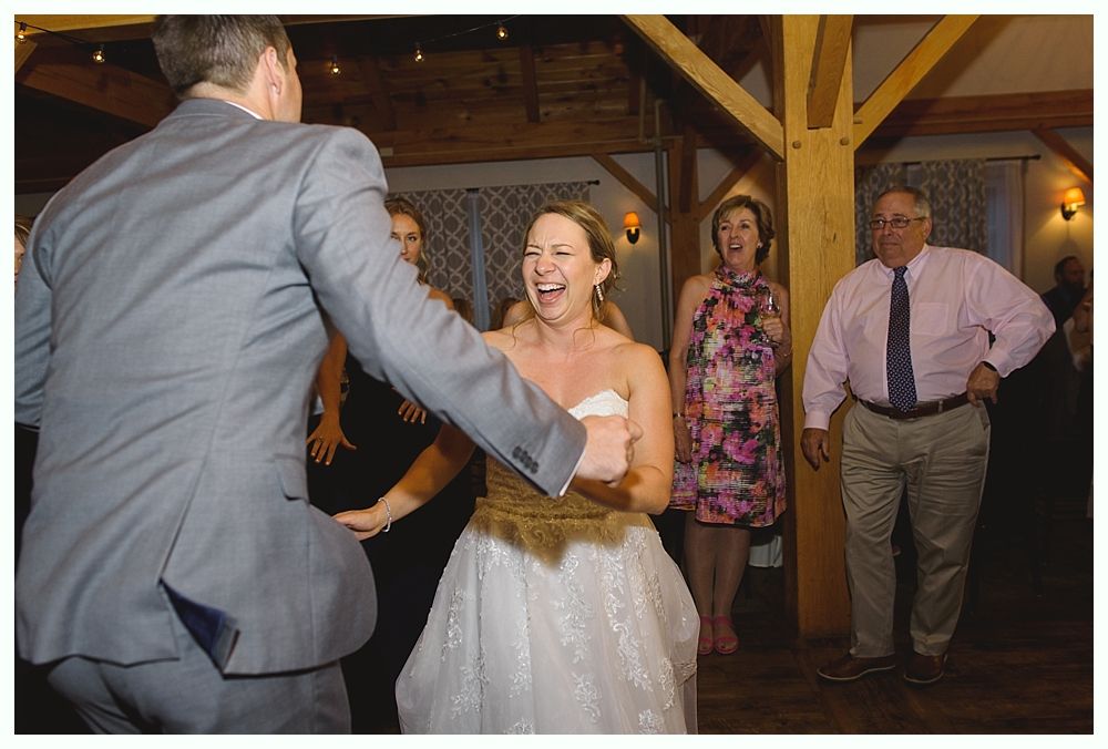 Bride dancing at wedding, wearing white dress with gold belt, smiling, with groom, and guests.