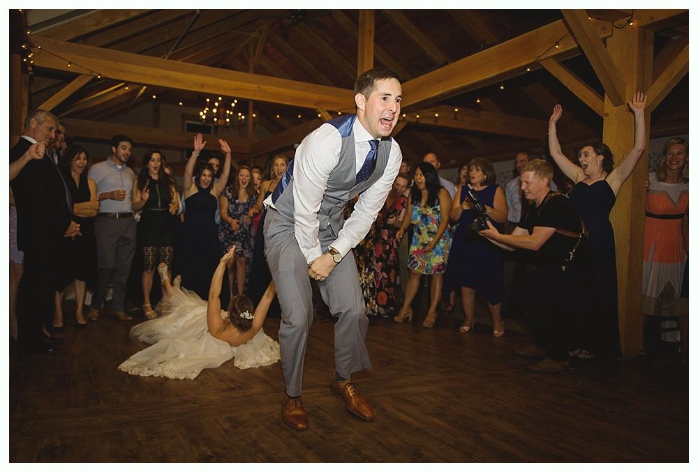 Groom jumps in excitement as bride bends backward during a wedding reception, many guests cheering.