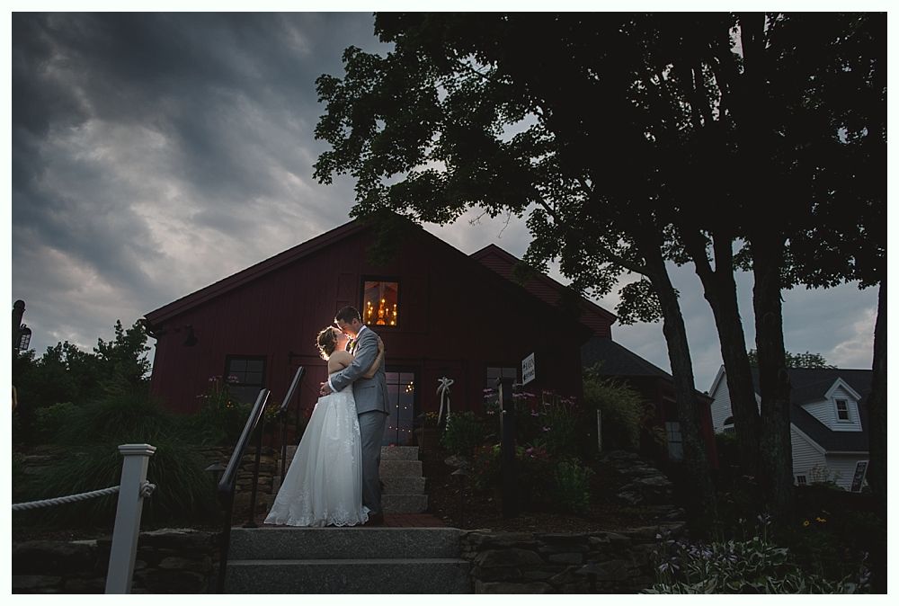 Couple kissing on steps of red building at dusk; backlit, dramatic lighting.