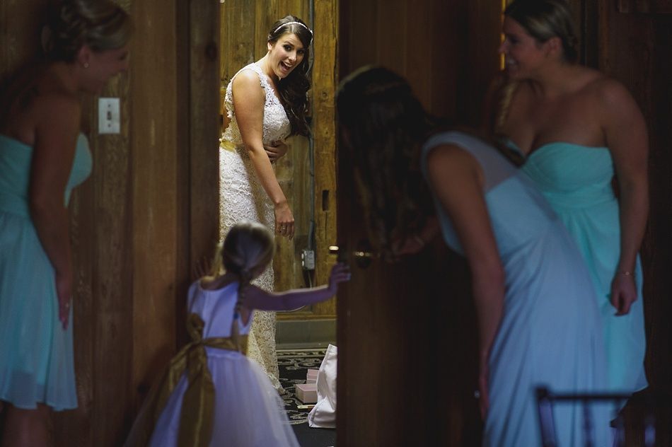 Bride in white dress opens door to bridesmaids in teal dresses. Flower girl stands nearby.