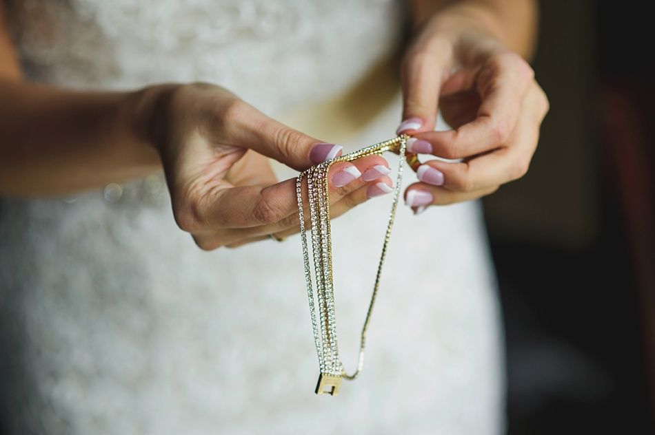 Woman in white dress holding a gold necklace with multiple strands; close-up.