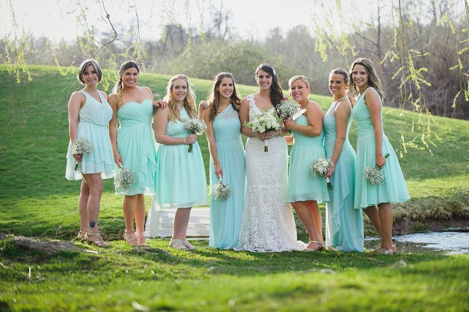 Bride and bridesmaids in mint dresses pose outdoors by a small pond.