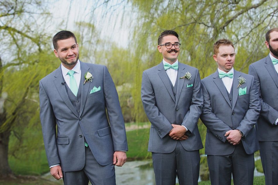 Men in gray suits with mint accents stand outside near a body of water.