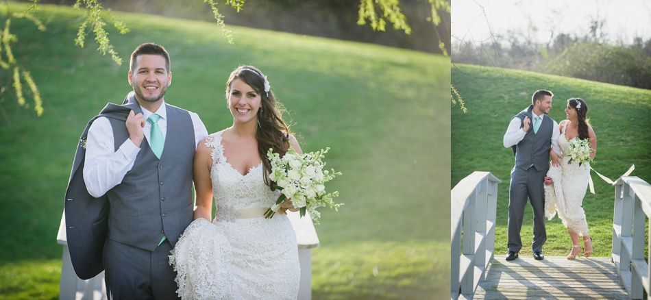 Wedding couple walking on a bridge. Groom in a grey suit, bride in white dress. Green grass and trees in background.
