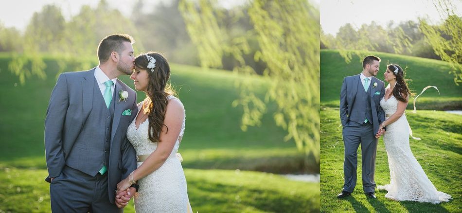 A newlywed couple embraces on a green golf course. The groom kisses the bride's forehead. Soft, natural light.