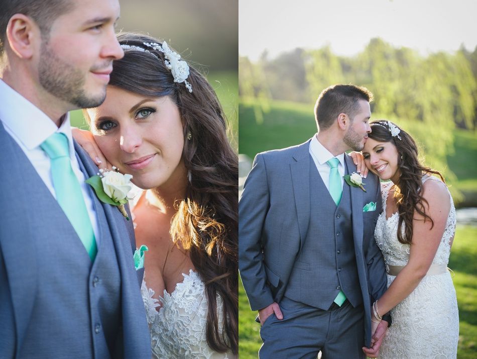 Bride and groom in formal attire, blue suit, mint tie, and lace dress, embracing outdoors, looking at the camera.