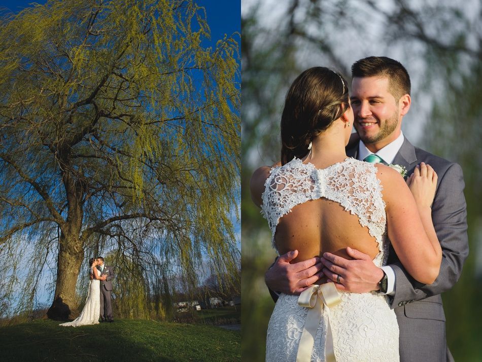 Wedding couple under a large willow tree and embracing, woman in lace dress, man in gray suit.