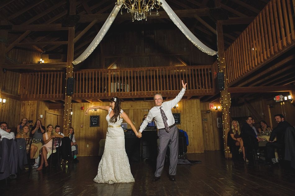 Bride and groom dancing at wedding reception in a wooden barn, holding hands, smiling.