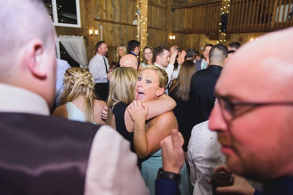 People dancing in a barn-like structure; a woman sticks out her tongue and hugs another person.