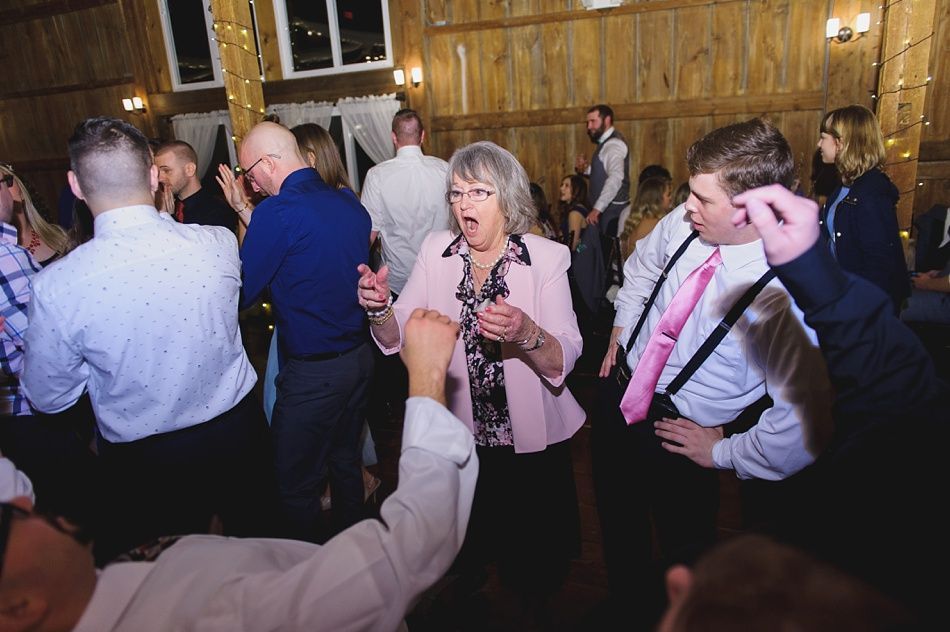 People dancing in a barn. Woman in pink jacket, gesturing; man with pink tie, dancing. Wooden interior with lights.