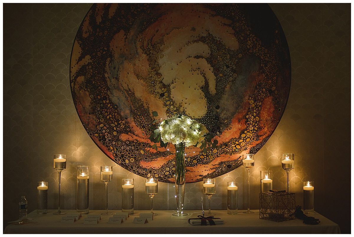 Wedding altar: Lit candles surround a bouquet in front of a circular artwork. Warm tones, soft light.