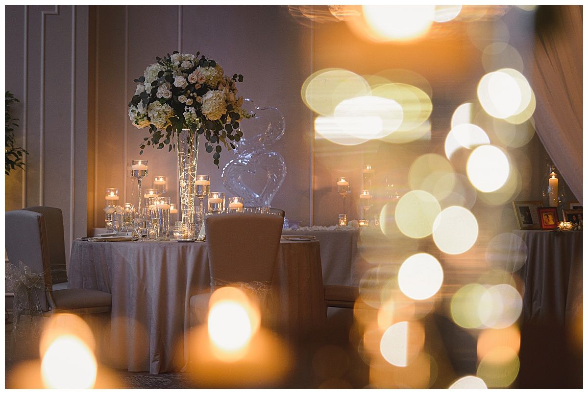 Elegant wedding reception table with floral centerpiece, candles, and soft lighting.