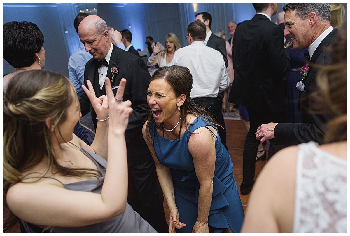 People dancing at a wedding reception; a woman in blue laughs, another makes a peace sign.