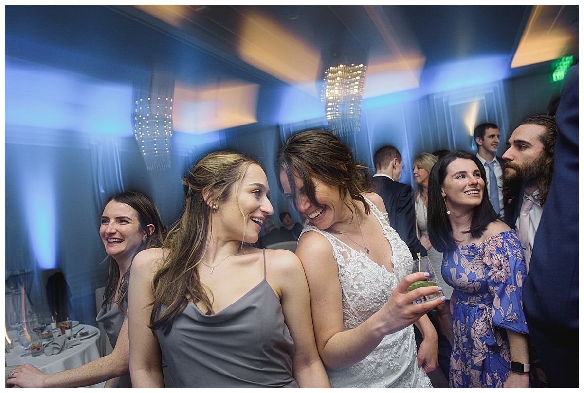 People dancing at an event, some smiling. Blue and gold lighting; chandelier in background.