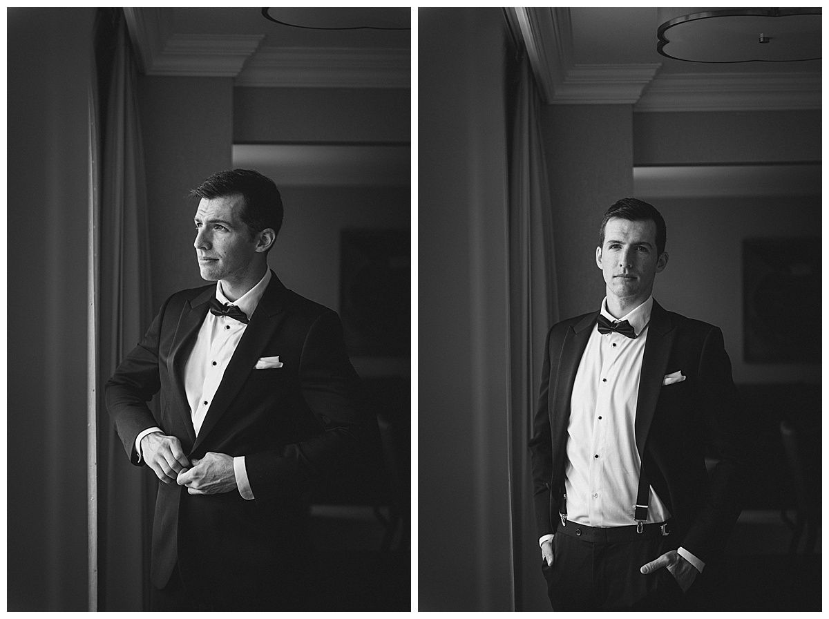 A man in a tuxedo adjusting his jacket by a window; black and white photograph.
