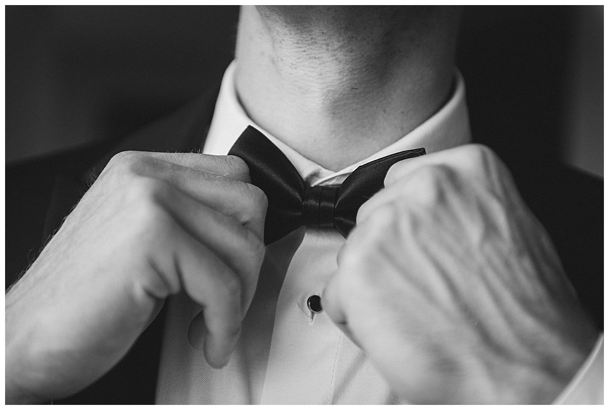 Man adjusting a black bow tie, formal attire, close-up shot.