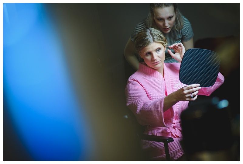Bride and groom embrace on a beach. Ocean, blue sky, and tree branch in the foreground.
