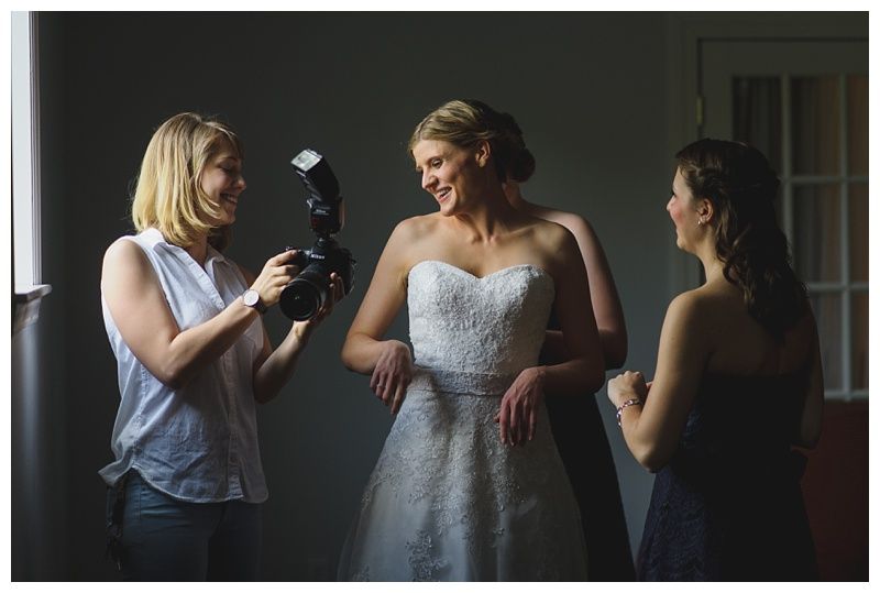 Bride and groom embrace on rocks by the ocean at sunset. The groom wears a blue suit, the bride a white dress.