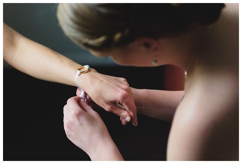 Bride with arms up, making a funny face, groom looking at his hand, cake cutting in background.