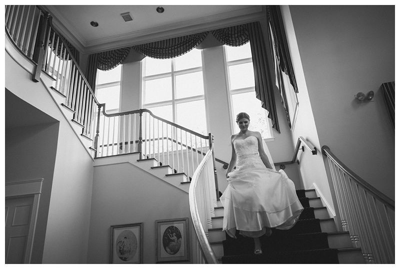 Bride with arms up, making a funny face, groom looking at his hand, cake cutting in background.