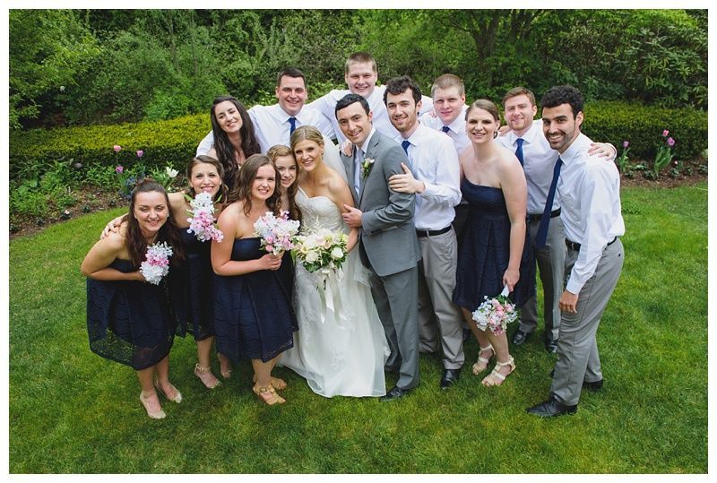Bride with arms up, making a funny face, groom looking at his hand, cake cutting in background.