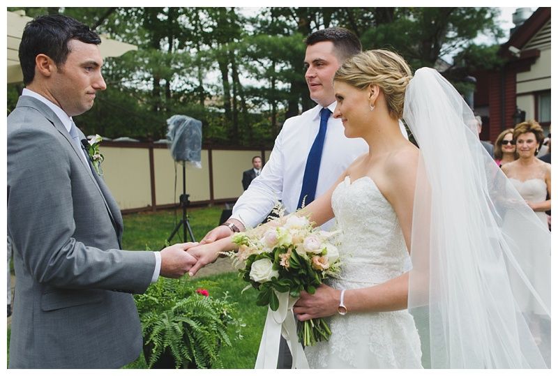 Bride with arms up, making a funny face, groom looking at his hand, cake cutting in background.