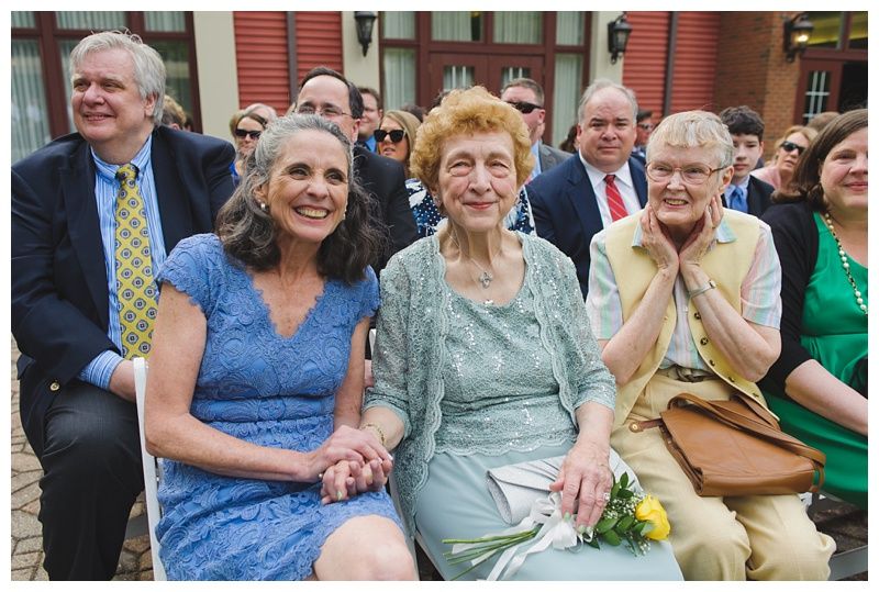 Bride with arms up, making a funny face, groom looking at his hand, cake cutting in background.