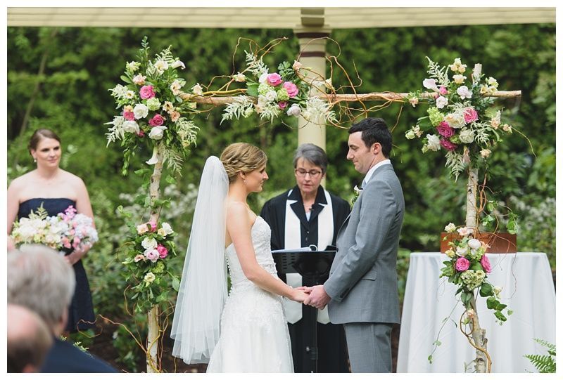 Bride with arms up, making a funny face, groom looking at his hand, cake cutting in background.