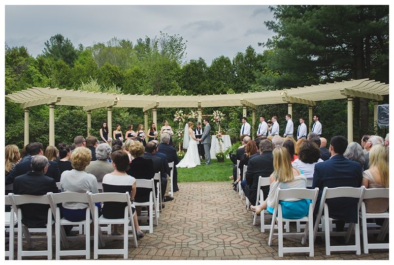 Bride with arms up, making a funny face, groom looking at his hand, cake cutting in background.