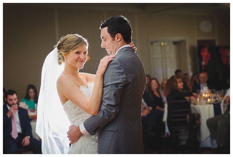 Bride with arms up, making a funny face, groom looking at his hand, cake cutting in background.