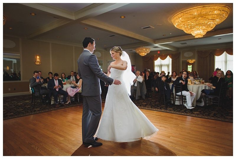 Bride with arms up, making a funny face, groom looking at his hand, cake cutting in background.