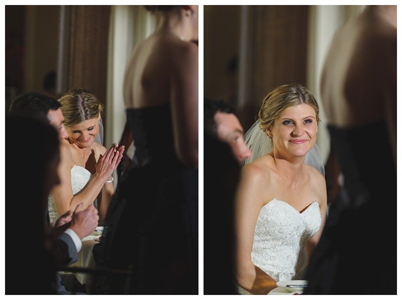 Bride with arms up, making a funny face, groom looking at his hand, cake cutting in background.