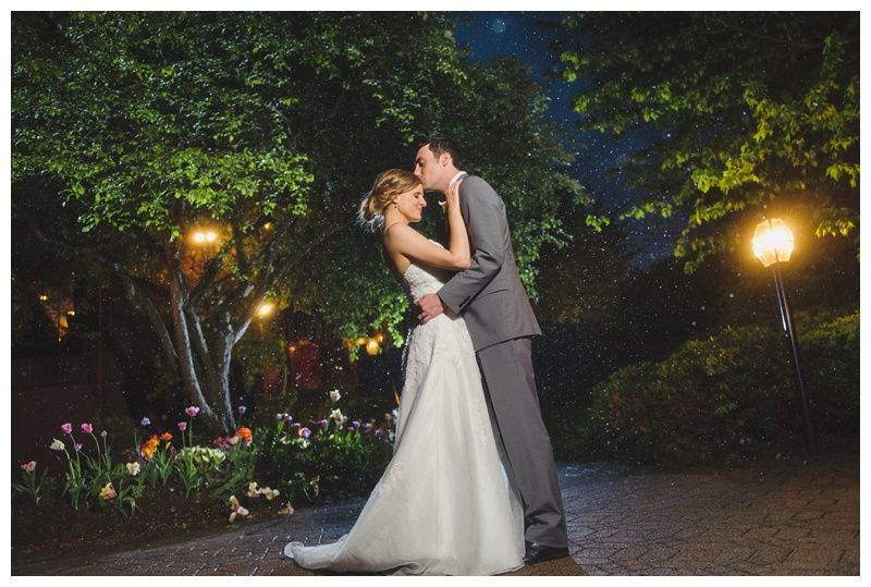 Bride with arms up, making a funny face, groom looking at his hand, cake cutting in background.