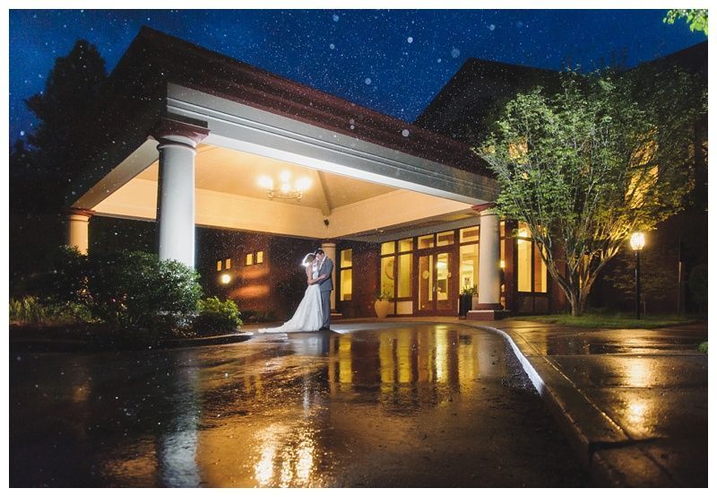 Bride with arms up, making a funny face, groom looking at his hand, cake cutting in background.