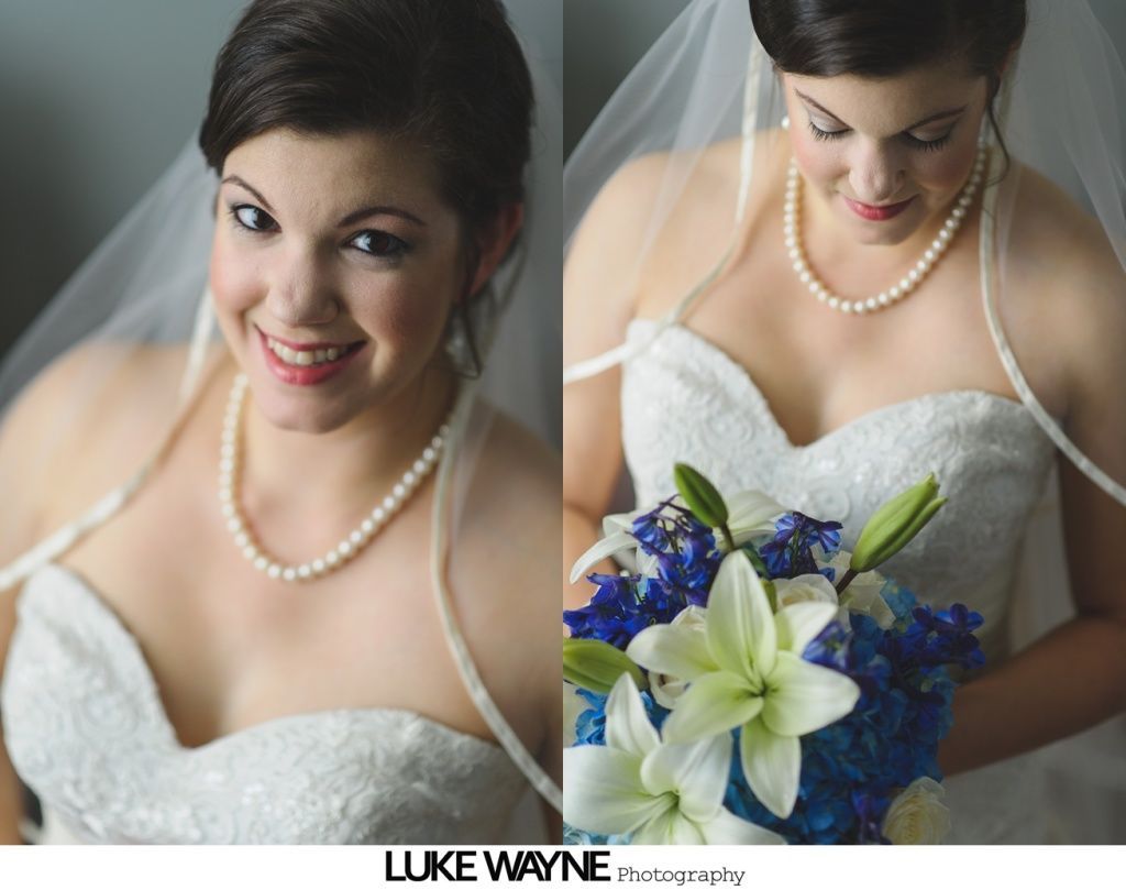 Bride in white dress, pearl necklace, holding blue and white bouquet.