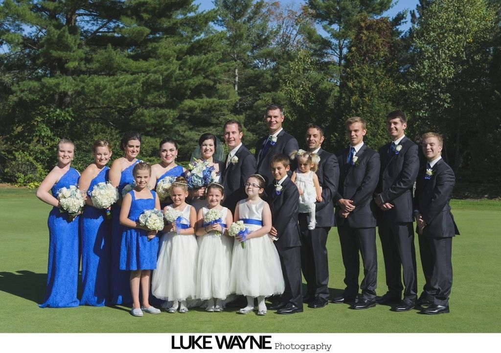 Wedding party poses on green grass. Bridesmaids in blue dresses, groomsmen in suits.