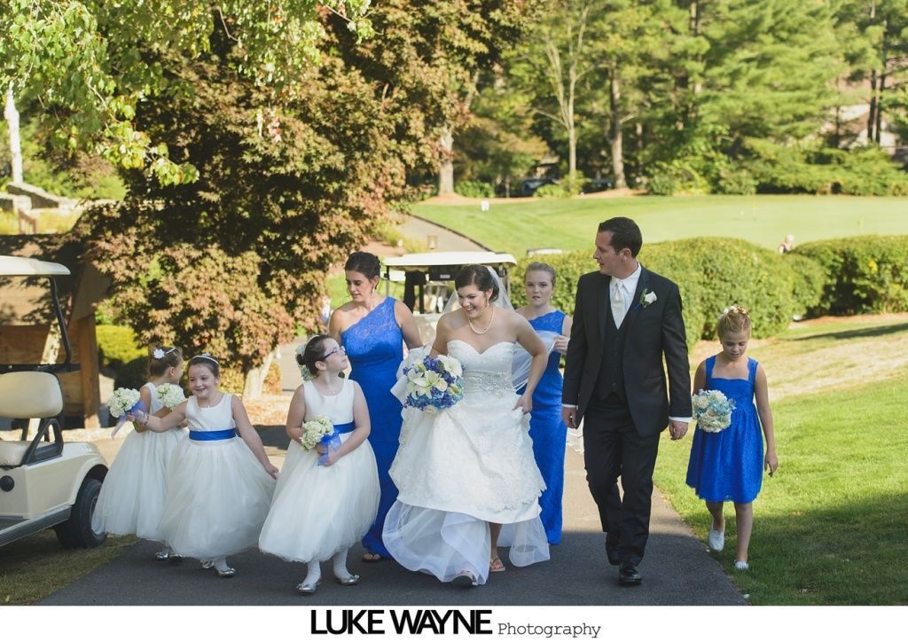 Wedding party walking on a path near a golf course. Bride, groom, bridesmaids in blue, flower girls.