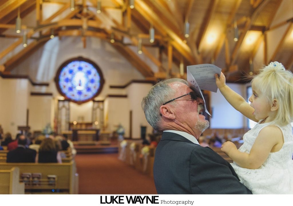 Little girl pours paper over man's face in a church during a wedding, interior shot.