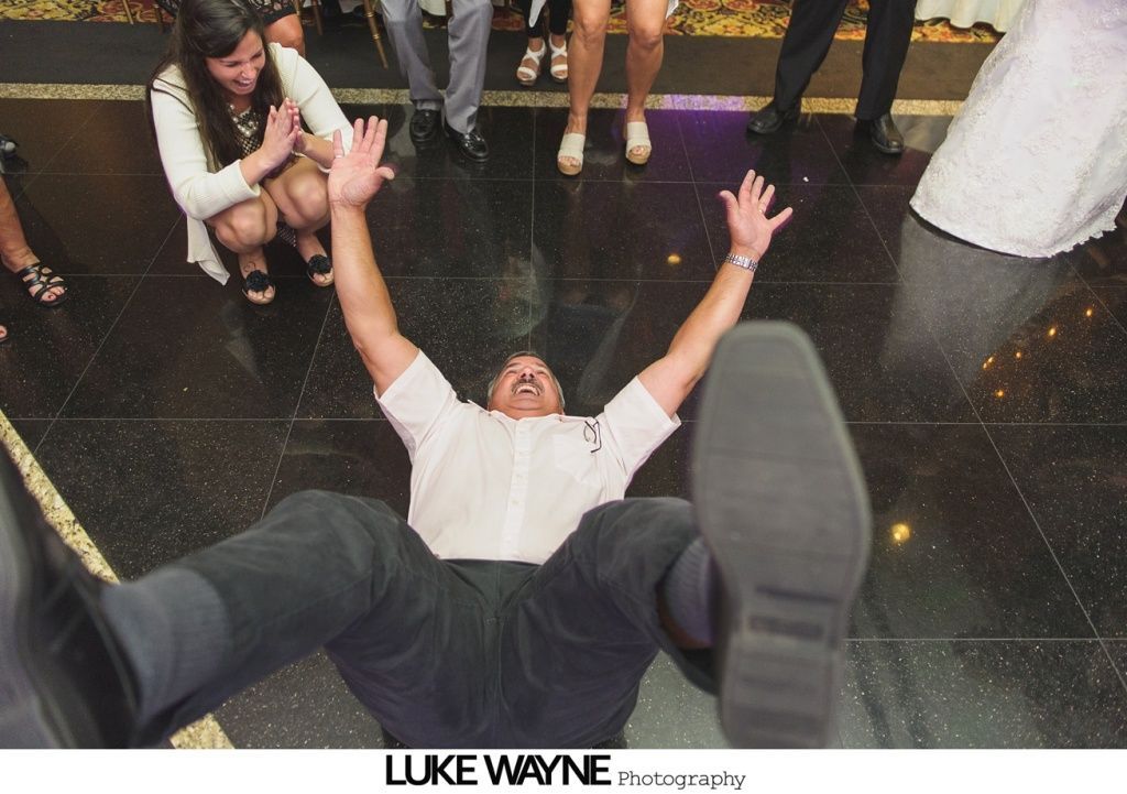Man falling backward on a dance floor, arms raised. People surround him at a celebration.