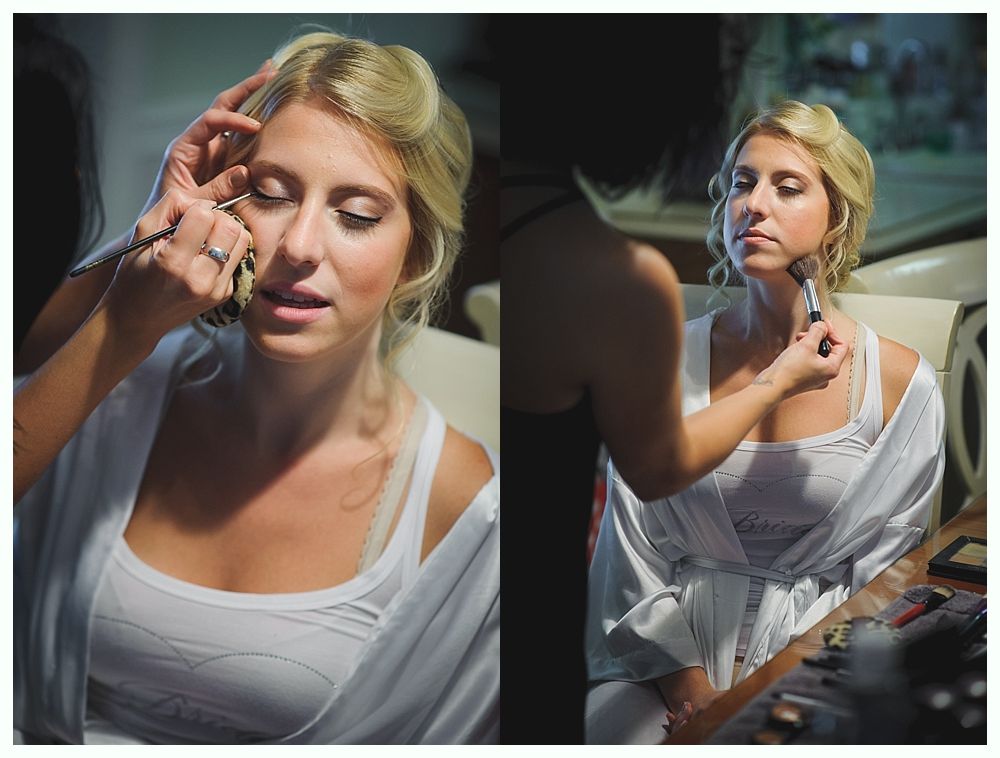 Bride and groom on rocky shoreline, ocean and blue sky background. Groom in suit, bride in white dress, looking at each other.