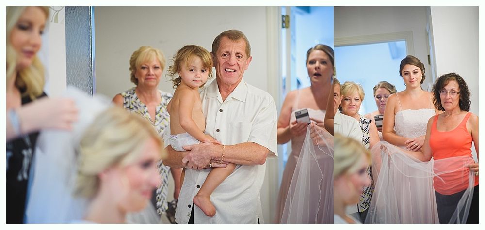 Bride and groom embrace on a beach. Ocean, blue sky, and tree branch in the foreground.