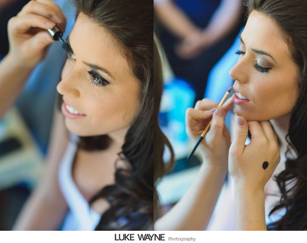 Woman getting makeup done: mascara applied to lashes, lip color being applied, soft lighting, getting ready.
