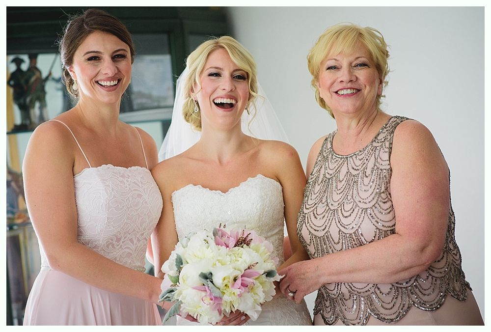 Bride with arms up, making a funny face, groom looking at his hand, cake cutting in background.