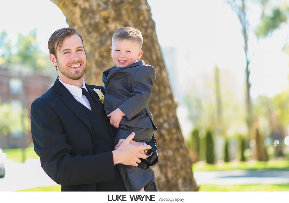Man in suit holds a smiling child in a matching suit outdoors.