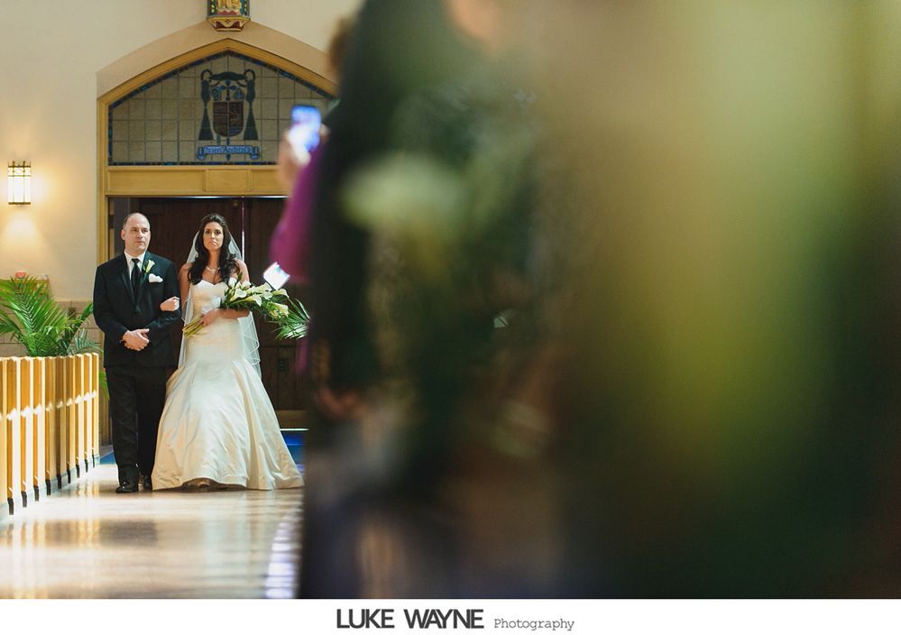 Bride walking down aisle with father; church setting, holding bouquet.