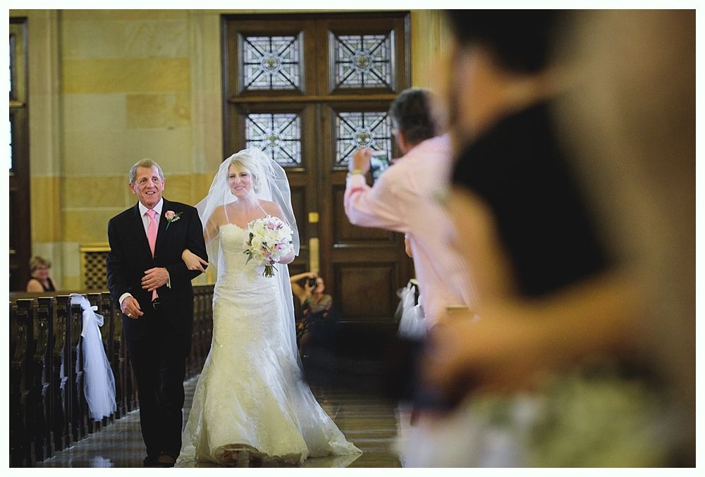Bride with arms up, making a funny face, groom looking at his hand, cake cutting in background.