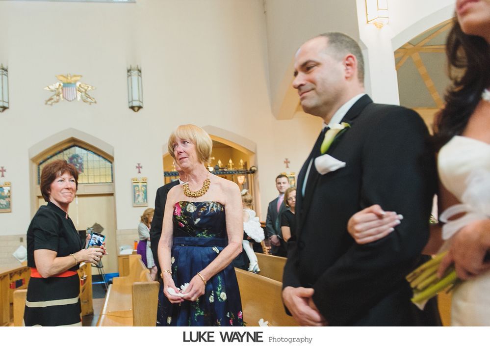 Groom in black suit with bride, walking down the aisle of a church; guests watch.