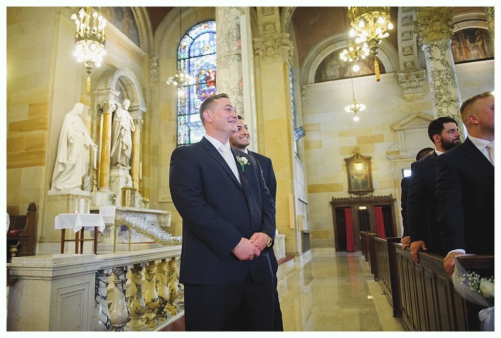 Bride with arms up, making a funny face, groom looking at his hand, cake cutting in background.
