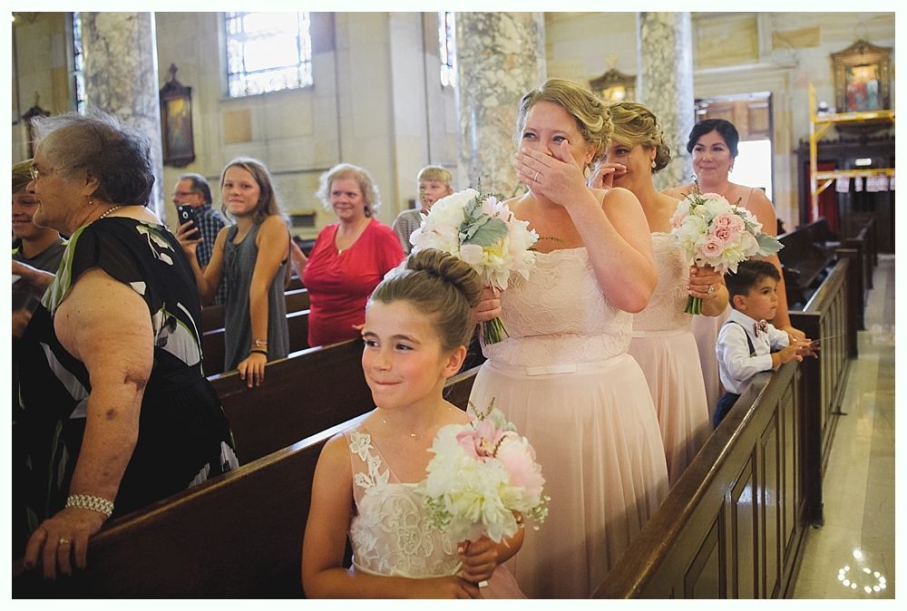 Bride with arms up, making a funny face, groom looking at his hand, cake cutting in background.